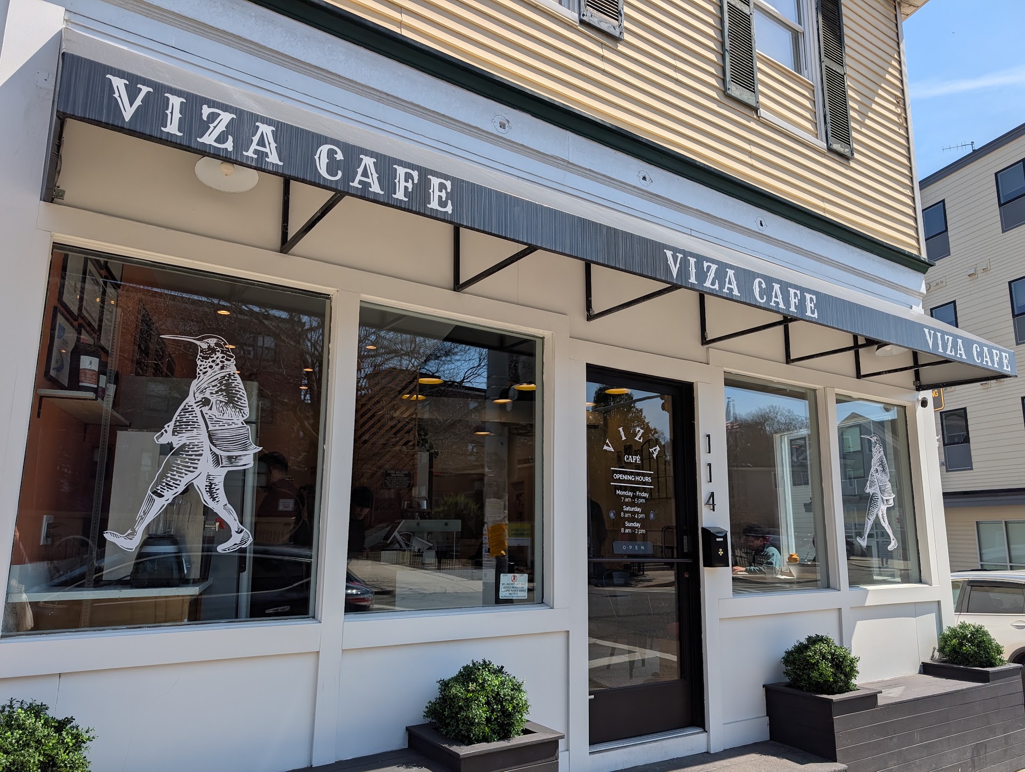 Viza Cafe storefront with dark striped awning and illustrated window figures